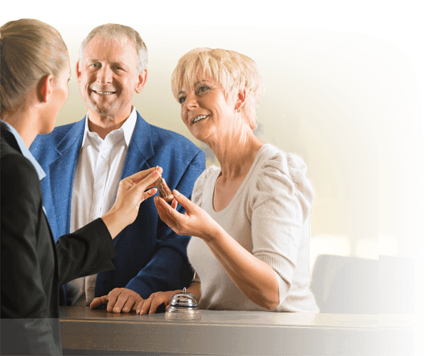 Senior couple checking in at a care facility reception desk assisted by a staff member — Independa improves staff efficiency