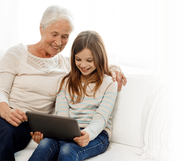 Grandmother and granddaughter sitting together on a sofa, smiling while using Independa on a tablet
